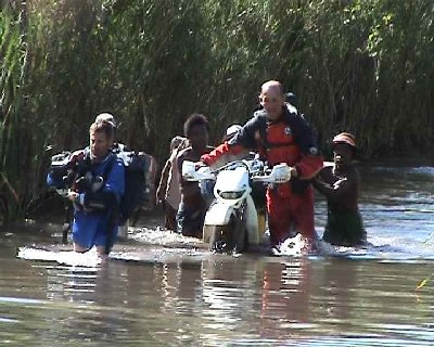 Cathy a trouvé une grande âme charitable  pour pousser sa moto dans le marigot pendant que Patrick traverse des bagages.